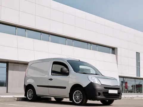 A small white service van parked beside a modern building
